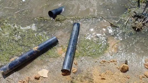 Northamptonshire Police Black plastic nesting tubes are both submerged and partly submerged in water on the edge of a lake's bank.
