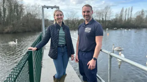 Shepperton Swan Sanctuary Ellie Vesey-Thompson and Danni Rogers at Shepperton Swan Sanctuary. They are standing on a jetty on a reservoir, both wearing blue outdoor summer clothing.