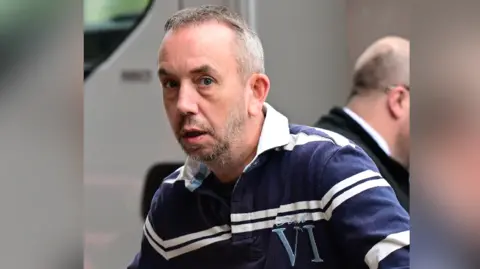 Wales News Service A man with a blue and white striped top, with short greying hair and a grey beard.