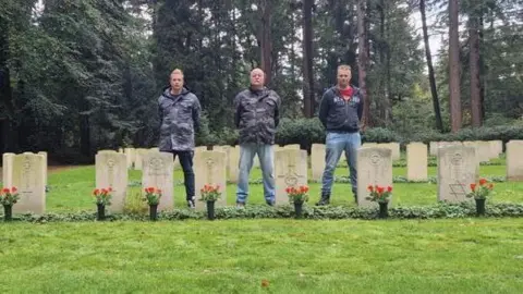 Family photo Brothers Kevin, Ron and Pim Klunder standing in front of the graves of service people who died during World War Two 