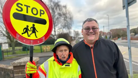 Brenda and her grandson Paul standing next to the zebra crossing where she worked for 40 years