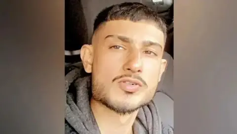 West Mercia Police A selfie of a man with dark hair and dark moustache and chin and jaw. He appears to be in a vehicle and is wearing a dark grey hoodie