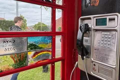 SUPPLIED A black telephone connected to a silver box in front of stained glass windows.