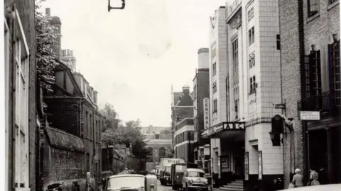 Mike Petty/Cambridge News Black and white photo showing Hobson Street in the 1960s with two cars, a parking meter and lamp on the left and on the right the cinema building, which has a sign on it saying Central Cinema ABC in capital letters