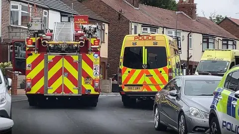 BBC A fire engine, police van and ambulance is within a cordon on a residential street after police discovered explosives in a man's house.