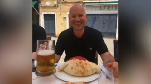 Harry Philp Alain Philp sat a table with a large pint of beer and a large calzone, wearing a dark top and smiling at the camera