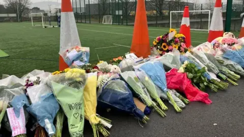 Dozens of bouquets of flowers have been left by the edge of a football pitch, many with handwritten messages in memory of Poppy.  