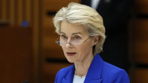 Getty Images A woman with blonde hair is wearing glasses, a blue jacket and white top