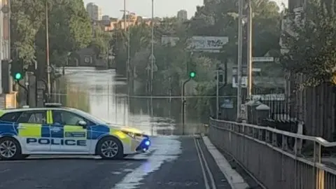 A police car parked across a flooded street.
