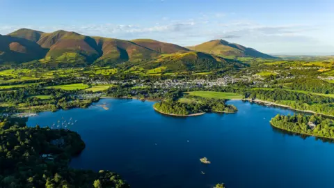 Getty Images Aerial view of Derwentwater - a large lake surrounded by greenery and rolling hills.