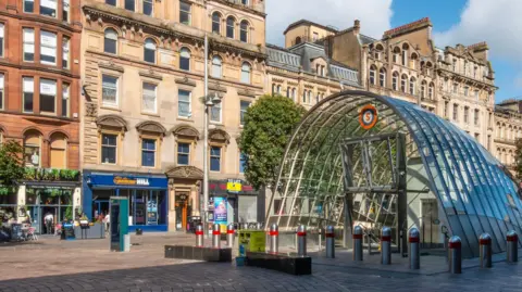 St Enoch Square in Glasgow surrounded by shops and businesses with a glass entrance to St Enoch Square in the centre.