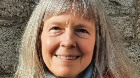 BBC The Reverend Dr Katherine Meyer - a close up shot where she is looking straight at the camera and smiling. She has long silver-blonde hair