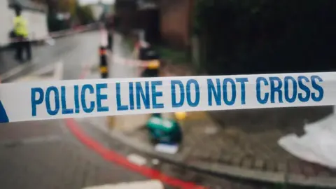 Police tape in front of what appears to be an accident in a street 