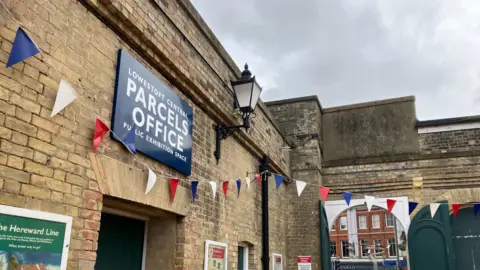 Guy Campbell/BBC Brick facade showing entrance to the former Parcels Office at the station which is now an exhibition space. Bunting can be seen hanging over a green door.