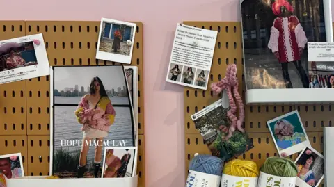 Two tan coloured clip boards, the one on the left has polaroid photographs and a magazine spread of people wearing Hopes clothes on it. The right clip board has a magazine spread in the top right corner, with more polaroid photographs and along the bottom are 3 bales of wool, coloured, blue, yellow and green. All infront of a pink back drop.