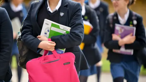 A number of school pupils wearing uniforms and carrying books and bags.