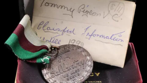 Laidlaw Auctioneers & Valuers The Dickin Medal awarded to Tommy is shown in a red velvet box. It has a red, green and white ribbon and there is a piece of paper tucked behind it.