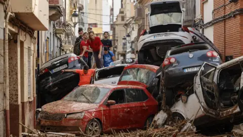 EPA People climb over piled up cars in the flood-hit municipality of Paiporta, Valencia province in Spain