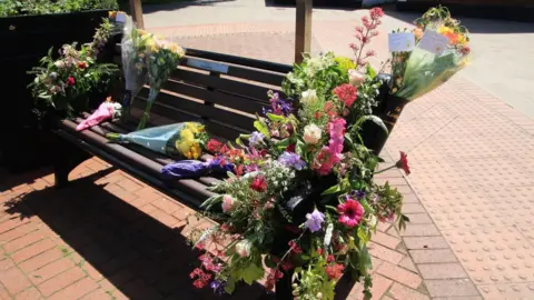 Ian Cuthbert A bench covered in bouquets of colourful flowers. 