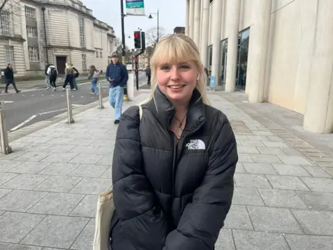 Marcie Niland-Sinyard, 19, smiles at the camera. She is stood outside the Cardiff university.