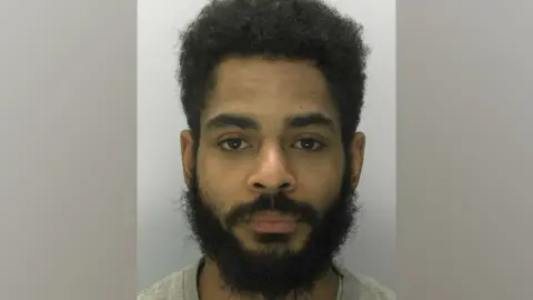 A mugshot of Claude Bond. He has short black hair and facial hair. He is pictured against a white background with a blank expression.