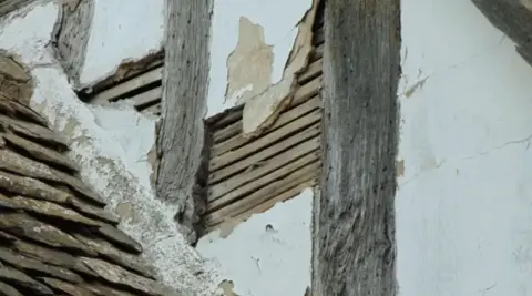 The Almonry Evesham A whitewashed wall with an exposed part showing wooden slats which sit underneath the plaster