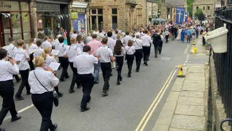 A brass band procession makes way through the streets.