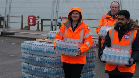 Southern Water Staff in high vis carrying large plastic bottles of water at a water station in Hastings on the seafront