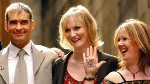 PA Media Tommy Sheridan with fellow MSPs Carolyn Leckie and Rosie Kane - Rosie Kane is holding up her hand, which has writing on it.