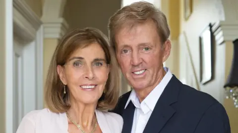 Family handout Judy Rock has shoulder length light brown hair and is smiling as Dickie Rock who is wearing an open necked white shirt and dark suit jacket hugs in close to her