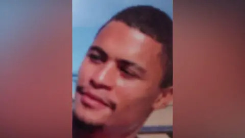 A man with black hair and a black moustache looks away from the camera.