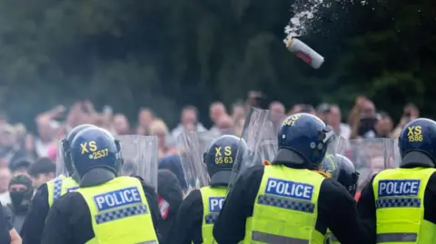 A can of lager can be seen hurling towards a group of police officers dressed in riot protection clothing at the Rotherham riot.