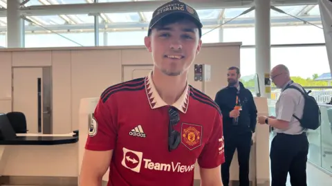 Davina Ramos/BBC Sam Winton has a current Manchester United shirt and is wearing a blue University of Stirling baseball cap.