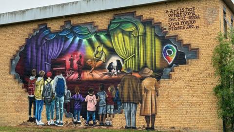 Mural shows people looking through hole in theatre wall at performers inside
