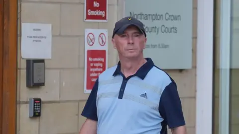 Jacob King/PA Raymond Connolly di luar Northampton Crown Court mengenakan kaos dan topi biru