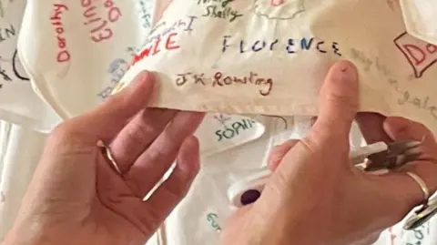 @LightninLex A pair of hands are holding a piece of fabric covered in embroided names. The one being held prominently to the camera is "JK Rowling"