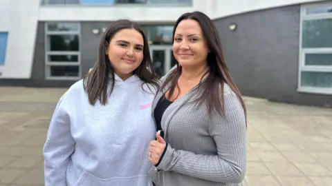 BBC A mother and her teenage daughter smiling at the camera. Both are wearing grey and have long brown hair. 