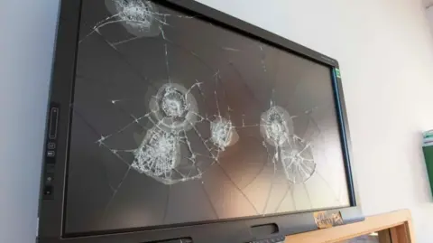 A TV hung on a wall is smashed in several places.