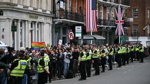 Getty Images A large crowd of people line the pavement of a city street. Police officers in high-viz vests are stood on the road next to the crowd in a row.