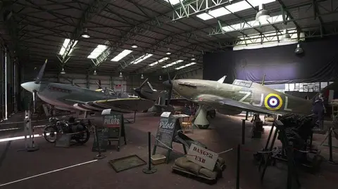 Spitfires and other aircrafts on display from World War Two in the Spitfire Visitor Centre - there are two planes in the image plus old World War Two signage about future pilots, plus a sign that reads Danger UXB