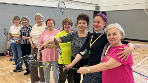 Group of women - all holding badminton rackets in their hands- smiling for the camera. 