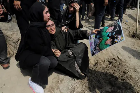 A woman holding a picture of children during funeral for victims following Israeli strike