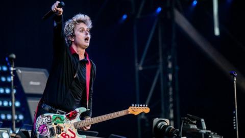 Green Day frontman Billie Joe Armstrong wings to the crowd with a pale green sticker decorated guitar