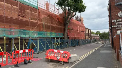 BBC A closed road in Blakenhall, with barriers and scaffolding on a factory that caught fire in January.