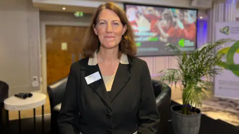 BBC Prof Beth Breeze smiles at the camera and behind her there is a presentation of philanthropy 