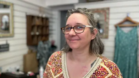 A grey-haired woman wearing glasses smiles at the camera.