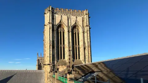 Solar panels on the roof of York Minster, with the sun shining against a blue sky.