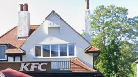 Close-up of KFC branch in West Wickham, showing the gable roof and top windows, as well as chimneys of the building