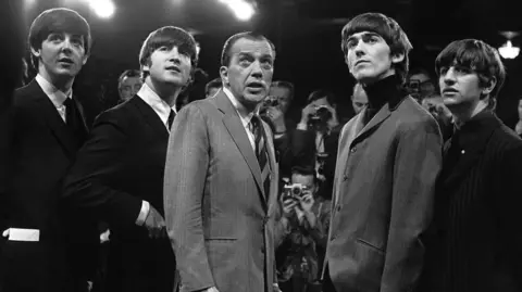 Getty Images The Beatles and US TV presenter Ed Sullivan on the set of the Ed Sullivan Show looking off-camera.