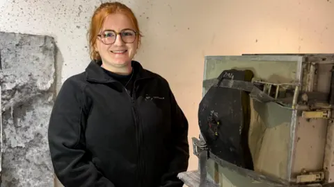 Seren stands next to a plate that has an impact mark on it from where it has been tested.